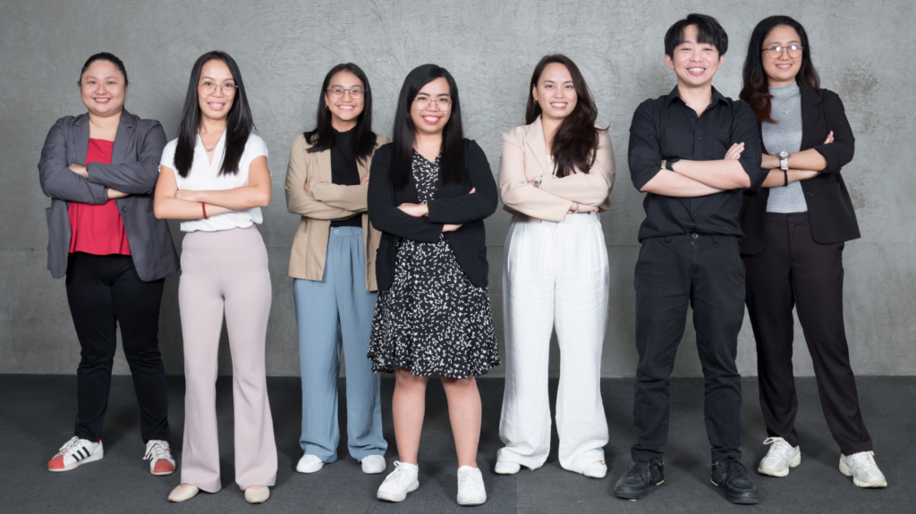 The editing team standing side by side with arms clasped, smiling confidently in their official group photo.