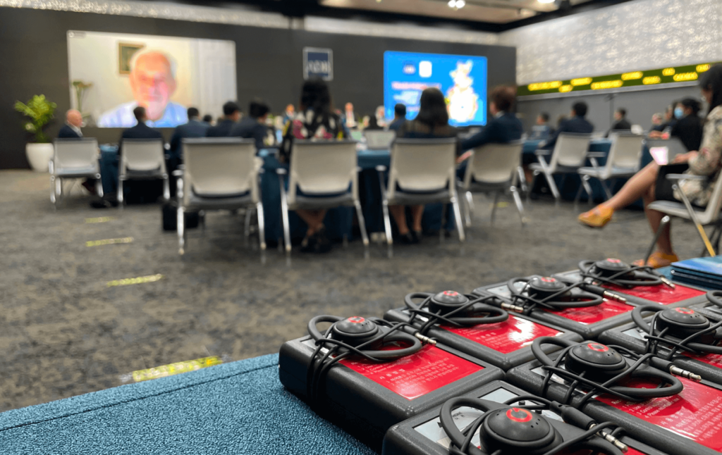 Conference attendees at a hybrid event with language interpretation devices in the foreground.