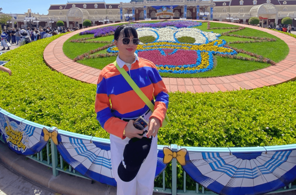 A woman standing in front of a Donald Duck flowery landscape.