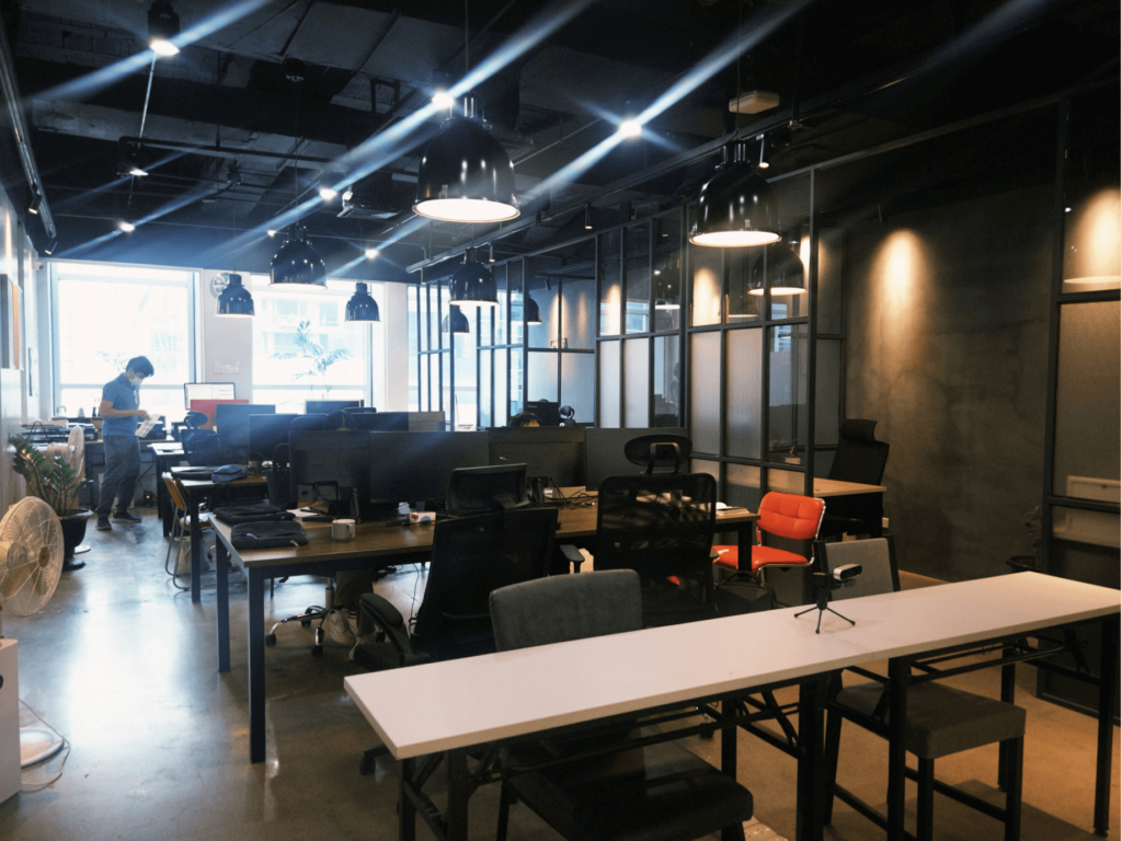 A contemporary open-plan office with empty desks and a person in the background.