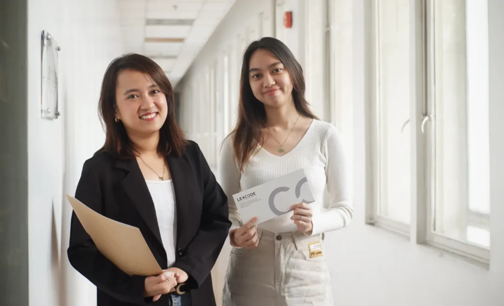 Ms. Andie and Ms. Dianne in front of Lexcode holding an envelope and folder