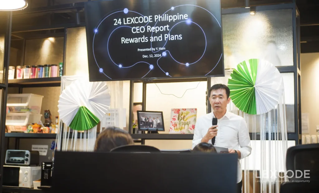 A man holding a microphone presents the 2024 Year-End Report in front of a crowd at the party.