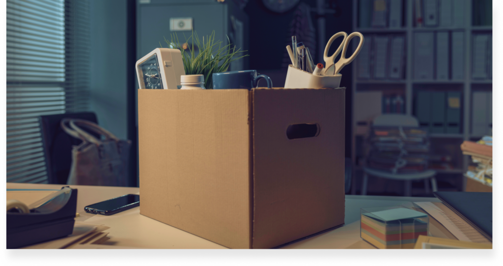 The belongings of an office worker piled in a carton box on top of a desk.