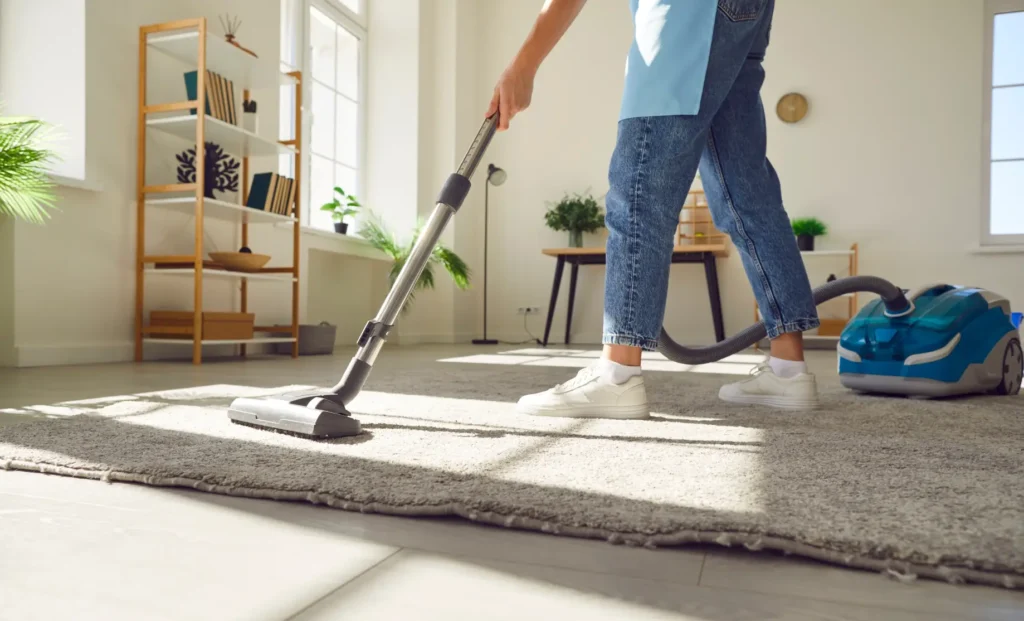 The person is vacuuming the carpet wearing jeans