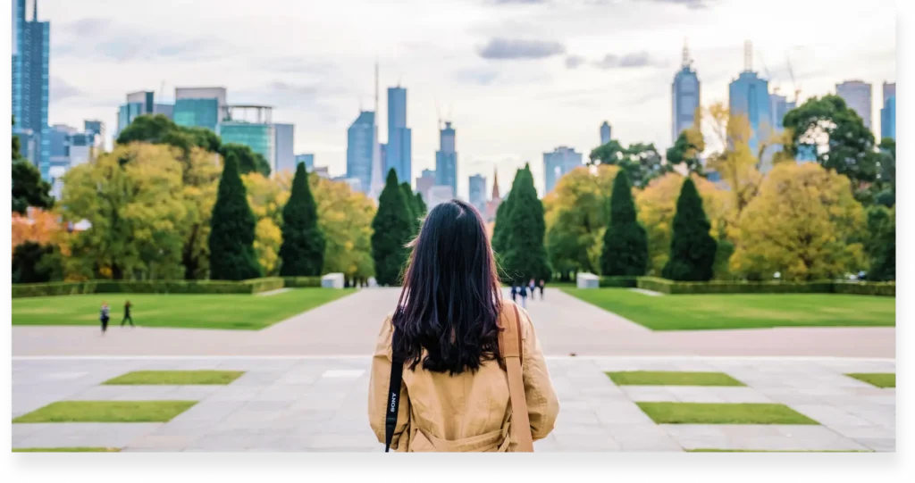 A young woman faces a large park with her back at the audience.