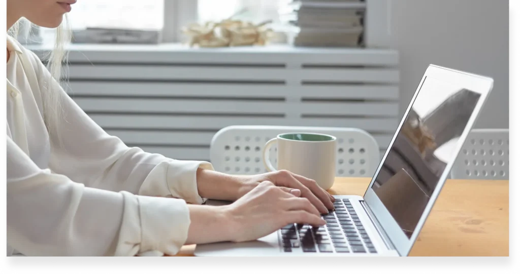 A young Lexcode editor in a white blouse typing on a laptop, refining content to shape impactful women's narratives.