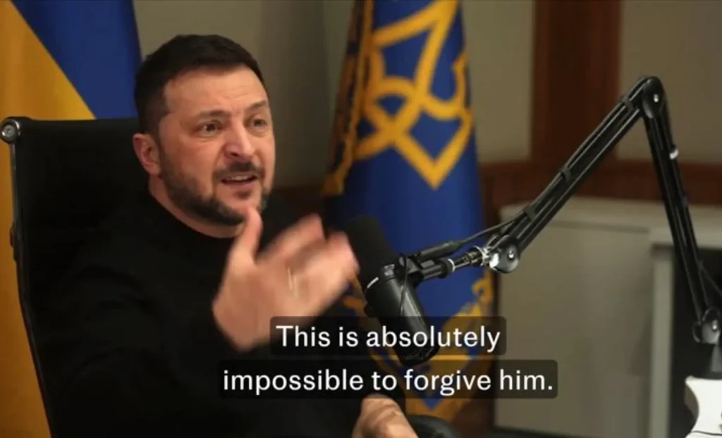 Ukrainian President Volodymyr Zelensky speaks into a podcast microphone with an expressive gesture. The Ukrainian flag and official symbols are visible in the background. A subtitle reads, “This is absolutely impossible to forgive him.”