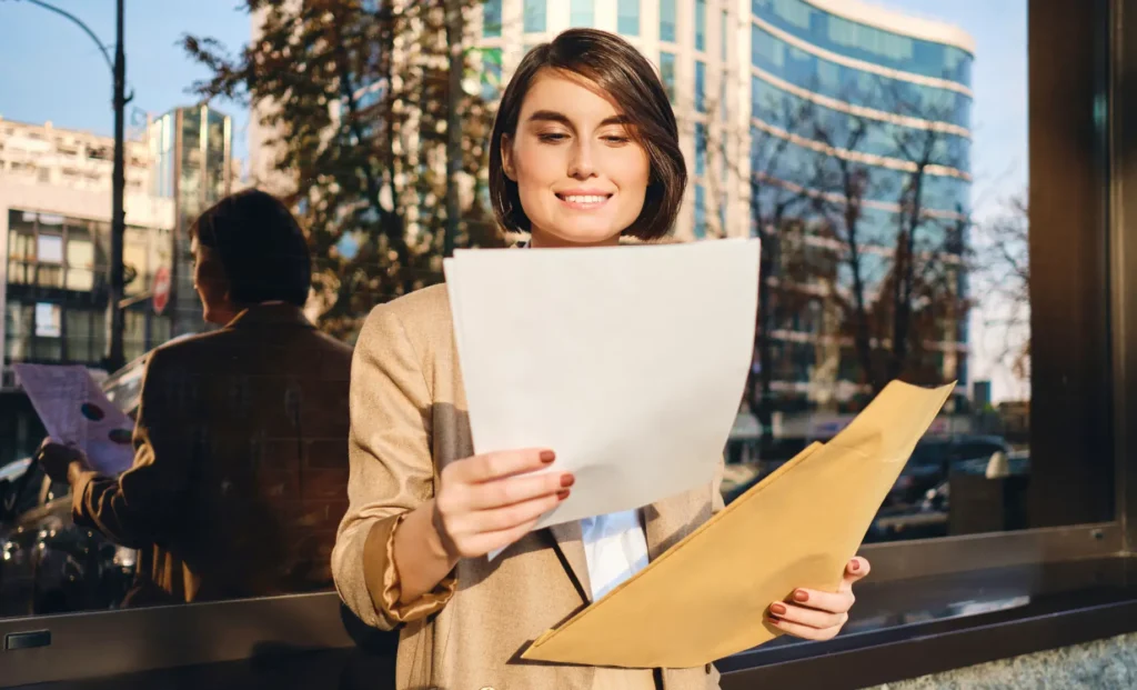 Young professional reviewing documents outside a modern office building.