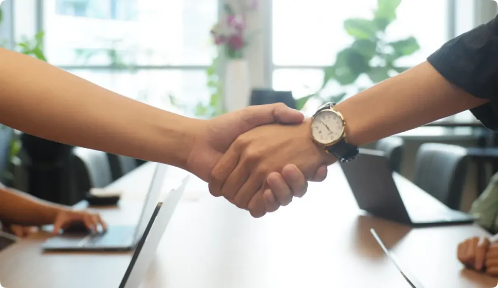 Two business professionals shaking hands across office table to seal partnership agreement or deal