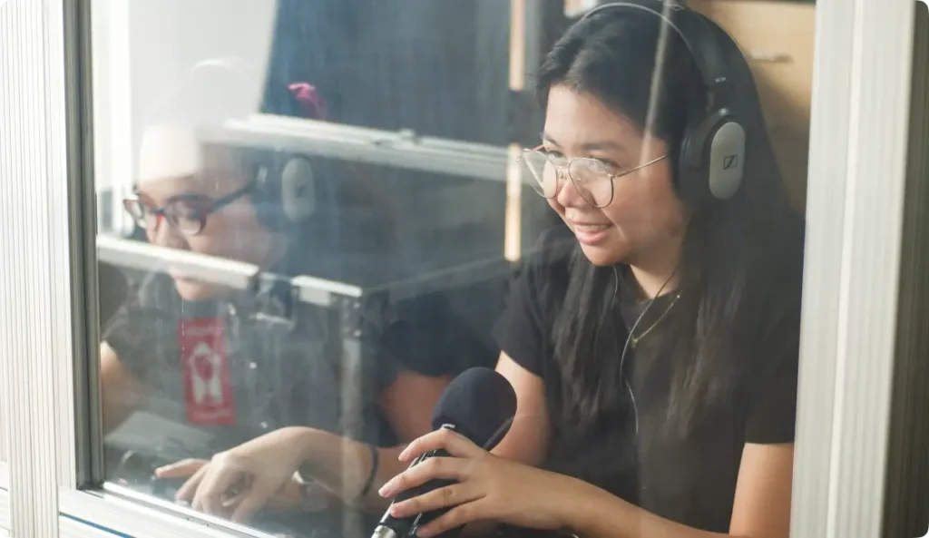 Professional female interpreter working in translation booth wearing headset and speaking into microphone