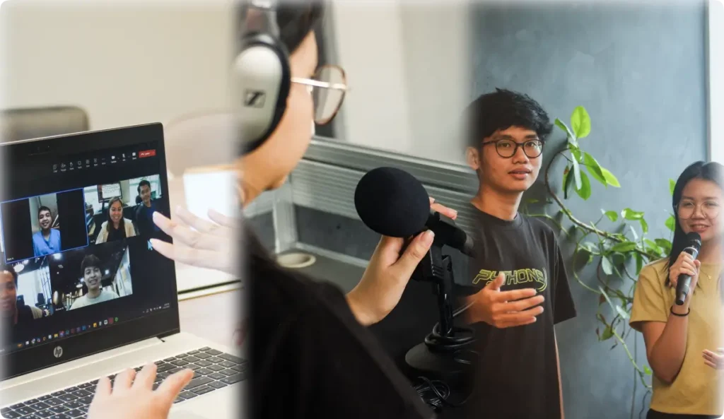 Young man holding microphone speaking to virtual audience on laptop screen while being filmed for hybrid event